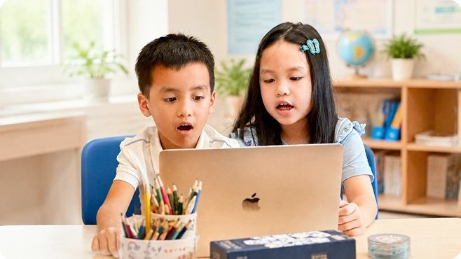 Hai em nhỏ, cậu bé áo trắng và cô bé áo xanh, ngồi cạnh nhau chăm chú nhìn laptop trên bàn có hộp bút màu — ảnh thẻ «Học sinh»