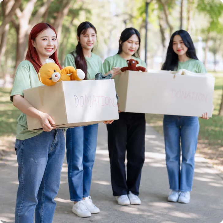 Bốn bạn trẻ ôm thùng quà và gấu bông đứng cạnh nhau ngoài trời — thẻ «Tổ chức xã hội và quỹ giáo dục»